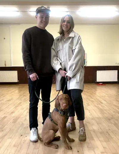 A young couple proudly posing with their young dog having completed a dog training class.